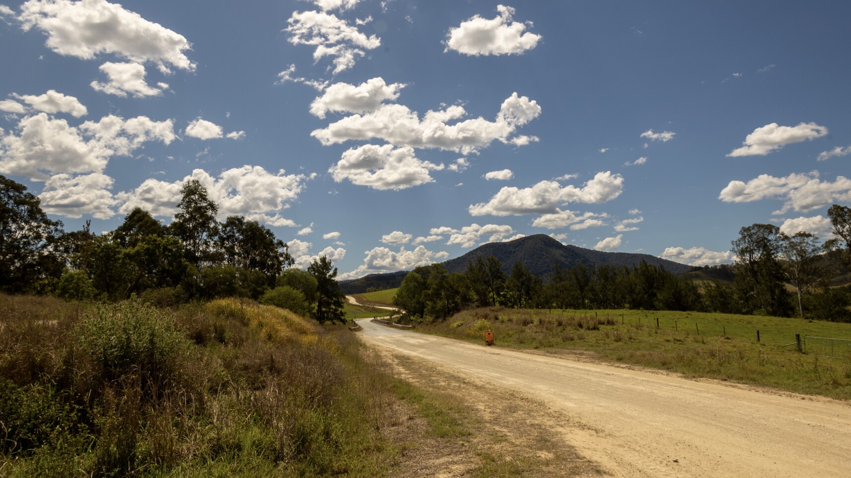 A dusty country road with hills and blue skies in the distance.