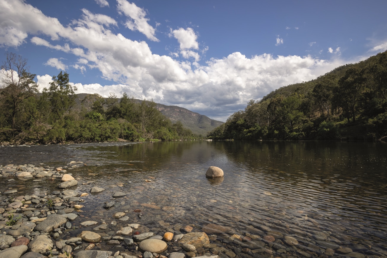 An image of the Macleay River with green hills and a cloudy sky in the distance.